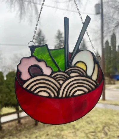 Stained glass suncatcher shaped like a red bowl of ramen with noodles, egg, and chopsticks