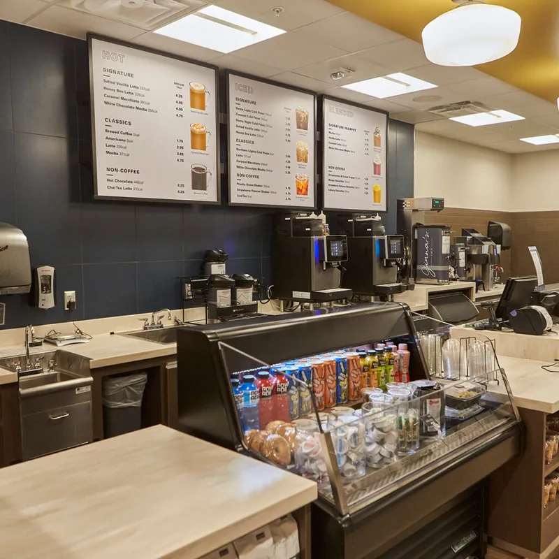 Coffee shop counter with digital menus for hot, iced, and blended drinks, espresso machines, and a refrigerated display case