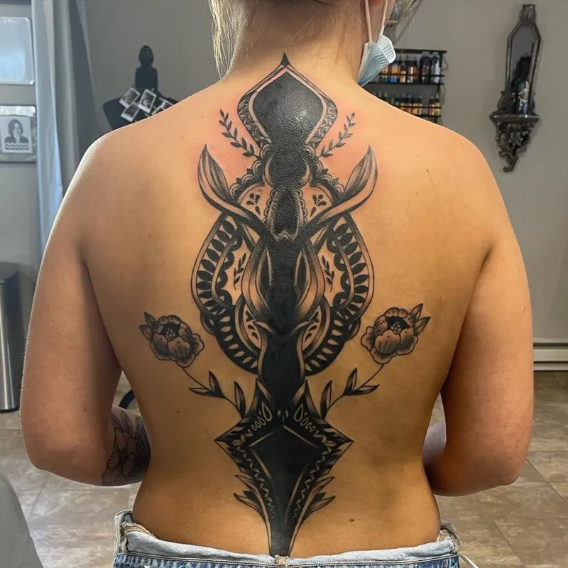 Large black-ink back tattoo featuring a deer skull, mandala-style patterns, and flanking flowers