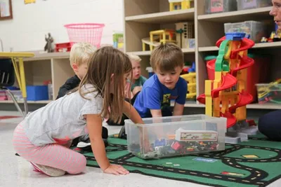 Young children playing with toys on a road-print rug in a colorful classroom