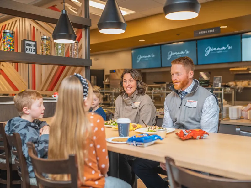 Two adults wearing name badges share a meal with three young children at a casual restaurant counter