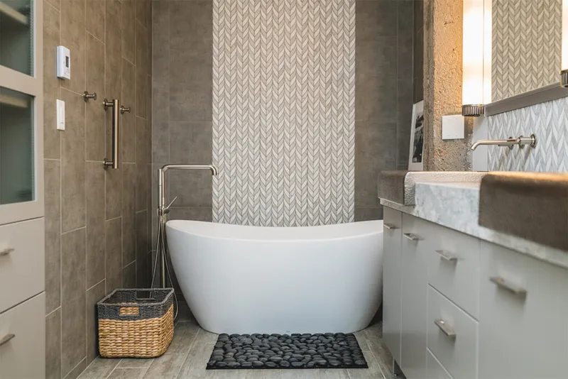 Freestanding white soaking tub beside herringbone tile accent wall in a renovated bathroom