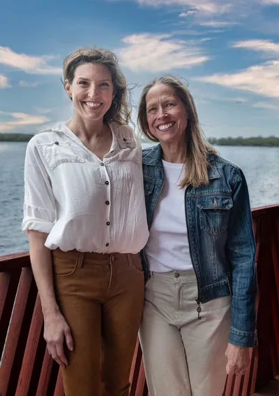 Two smiling women standing together on a red dock overlooking a lake