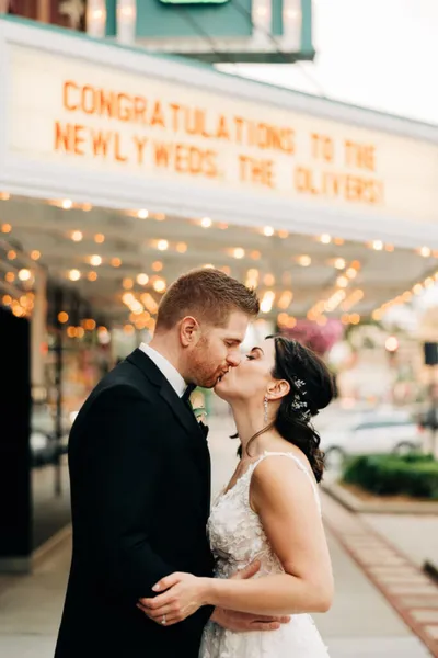 Bride and groom kissing beneath a lit marquee reading 'Congratulations to the Newlyweds, The Olivers!