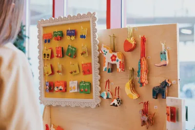 Person browsing colorful ceramic earrings and animal ornaments displayed on boards at a craft market