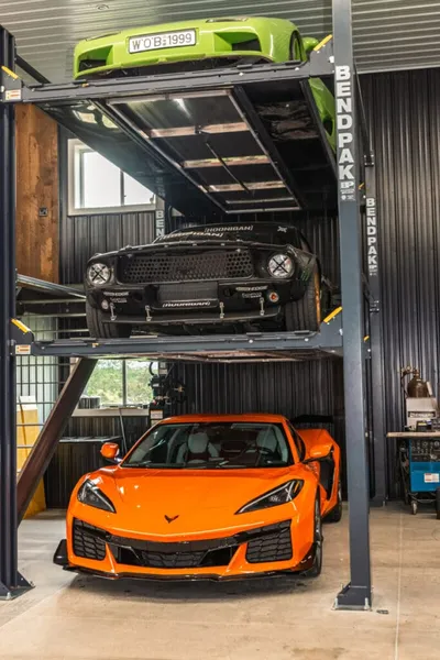 Three sports cars stacked on a BendPak car lift inside a private garage