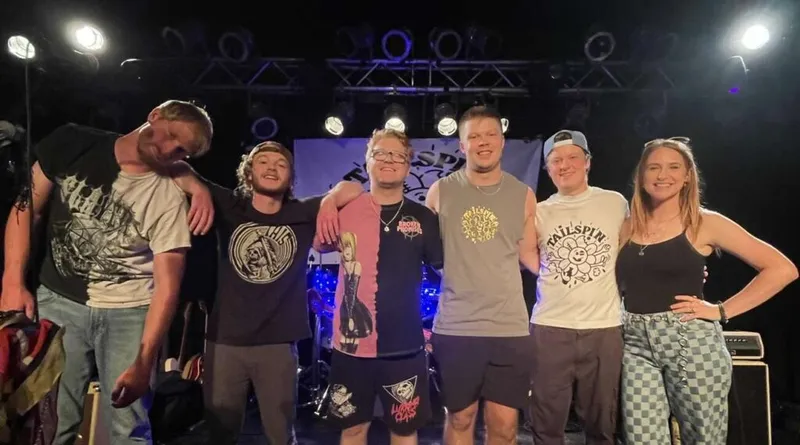 Six young people posing together on a small stage under purple stage lights