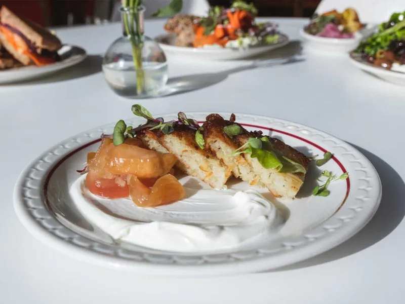 Plated crispy cakes with creamy sauce, tomato compote, and microgreens on a white restaurant plate