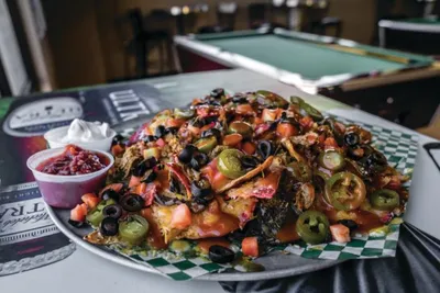 Large loaded nachos piled with jalapeños, black olives, tomatoes, and sauce on a white plate