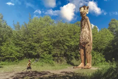 Towering wooden troll sculpture beside a person in a forest clearing under blue sky