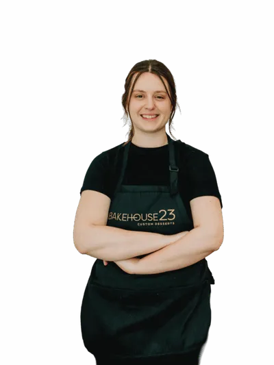 Smiling woman in black shirt and dark green Bakehouse 23 apron, arms crossed