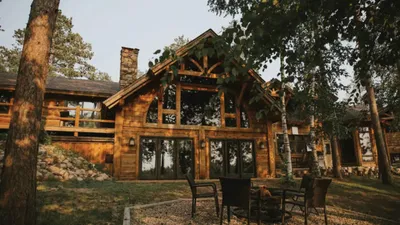 Rustic log cabin lodge with large windows and timber frame gable, surrounded by trees