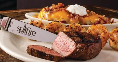 Sliced grilled steak with shrimp and a loaded baked potato on a white plate