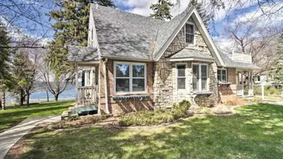 Stone cottage with steep gabled roof and green lawn near a lake