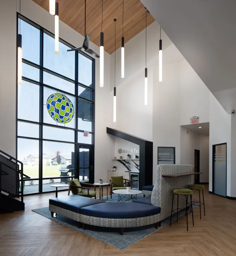 Modern office lobby with soaring wood-paneled ceiling, tubular pendant lights, and blue sectional seating near