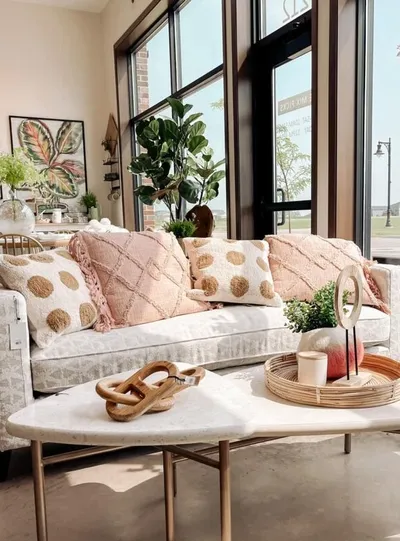 White sofa with blush and gold throw pillows beside tall windows and a marble coffee table