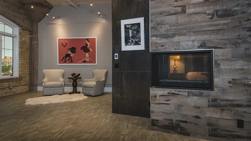 Loft condo interior with reclaimed wood fireplace wall, two armchairs, and bold red artwork