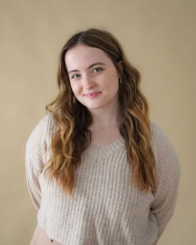 Young woman with long wavy brown ombre hair wearing a cream knit sweater against a beige background