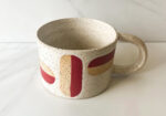 Handmade ceramic mug with red and tan abstract brushstroke pattern on speckled white clay