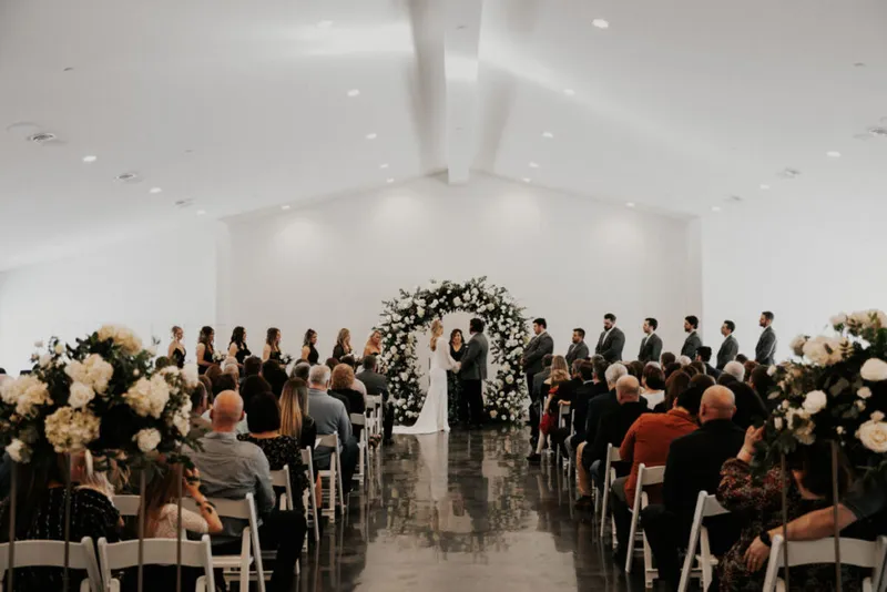 Wedding ceremony in a bright white venue with a floral arch and seated guests