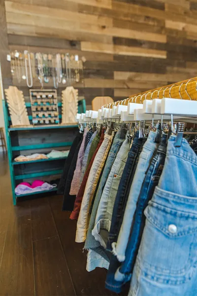A rack of denim and colorful jeans in a boutique with a teal shelving unit and jewelry display behind