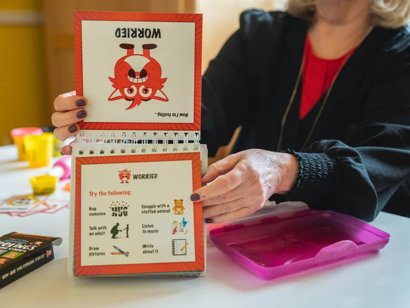 Adult holding open a children's feelings flip chart showing a 'Worried' monster illustration and coping tips