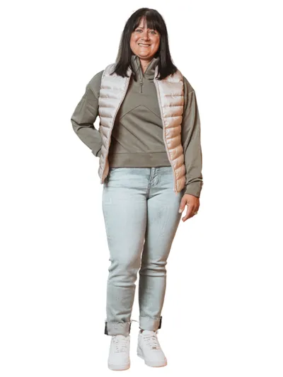 Smiling woman in a puffer vest, olive hoodie, light jeans, and white sneakers