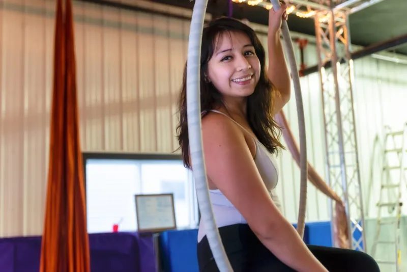 Smiling young woman gripping aerial rope apparatus inside a training studio
