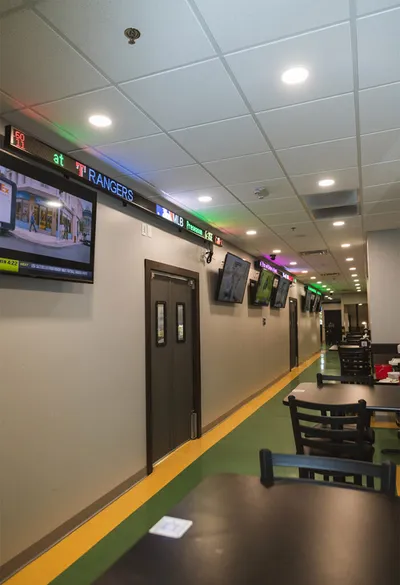 Indoor dining corridor with TV screens and LED score tickers along the wall