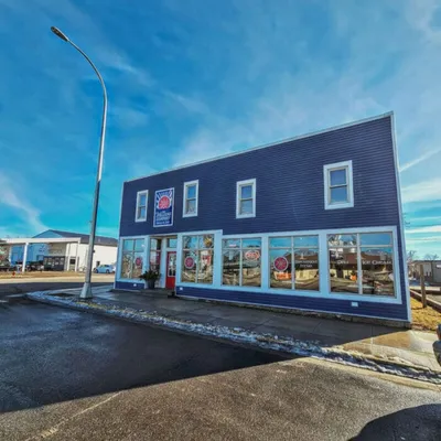 Two-story navy blue commercial building with large storefront windows and a wet parking lot under a bright blue sky