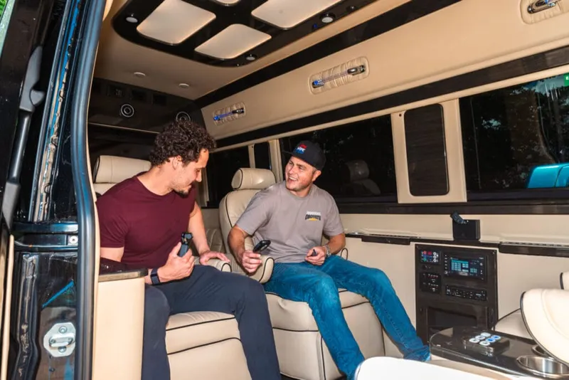 Two men chatting inside a customized van with cream leather seats and a skylight roof