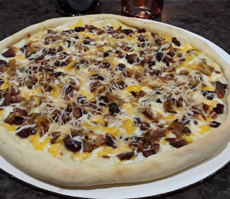 Whole pizza topped with melted cheddar, white cheese, bacon, and caramelized onions on a round pan