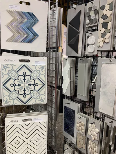 Tile sample boards displayed on a wire rack, showing mosaic, patterned, and stone styles