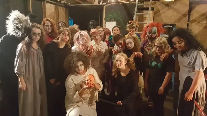Large group of people in horror costumes and gore makeup posing inside a haunted attraction