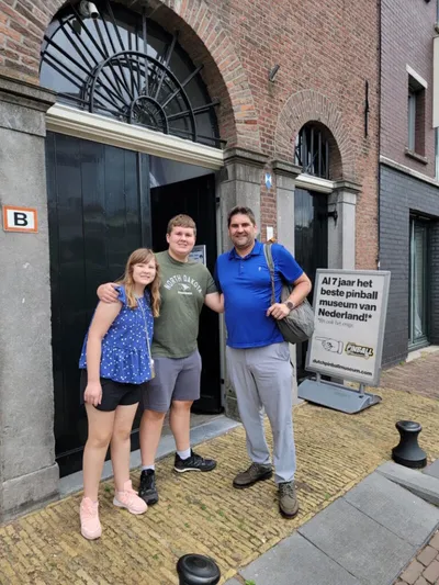 Three people pose smiling outside a brick building with a pinball museum sign