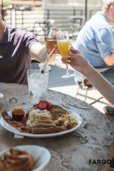 Two people clinking mimosas over a brunch plate on a sunny outdoor patio