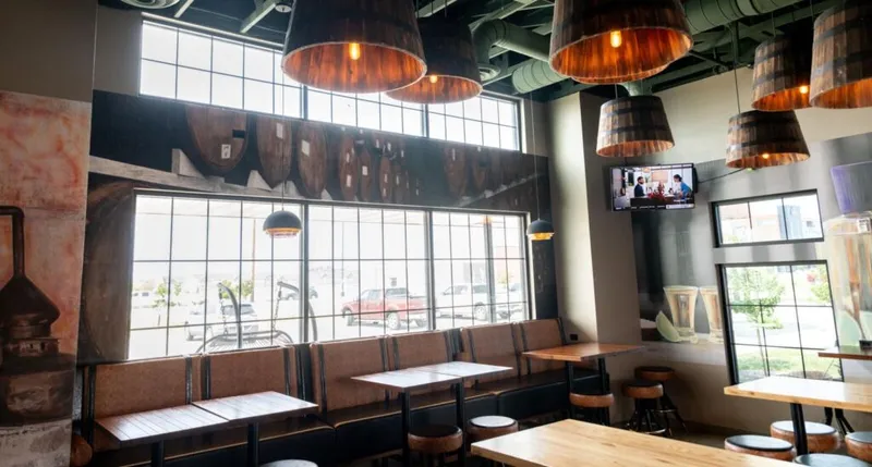 Restaurant interior with barrel-shaped pendant lights, booth seating, and large industrial windows