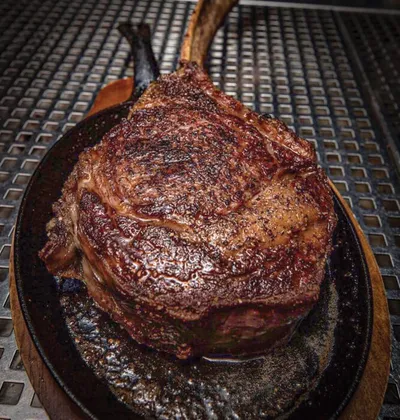 Seared tomahawk ribeye on a cast iron skillet over a metal grate