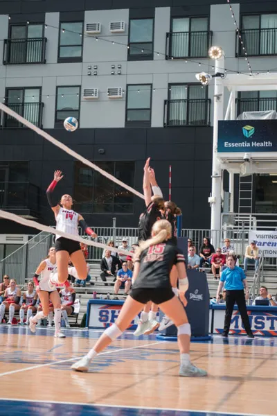 Player in white jersey #14 leaps to spike volleyball over the net at an outdoor court