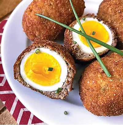 Scotch eggs with soft yolk centers on a white plate, garnished with chives