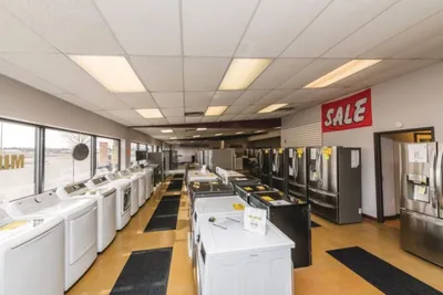 Appliance showroom floor with washers, dryers, and refrigerators under a red Sale banner