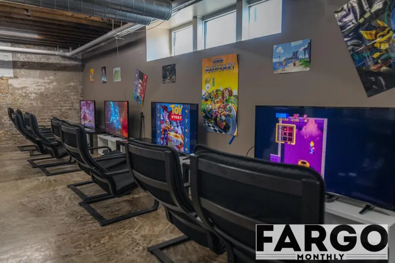 Row of gaming chairs facing flat-screen TVs with colorful video game posters on a gray wall