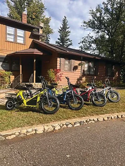 Four fat-tire electric bikes lined up on a grass strip in front of a wood-sided lodge