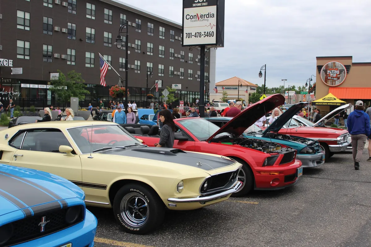 Classic and modern Mustangs lined up at an outdoor cruise night car show on a busy downtown street