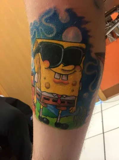 Colorful SpongeBob SquarePants tattoo wearing sunglasses on a person's forearm