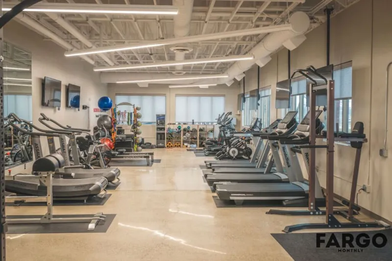 Spacious corporate fitness center with treadmills, rowing machines, and free weights under exposed white ceiling