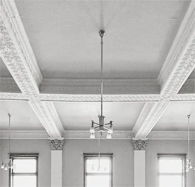 Ornate plaster ceiling with coffered beams and a hanging chandelier above tall windows