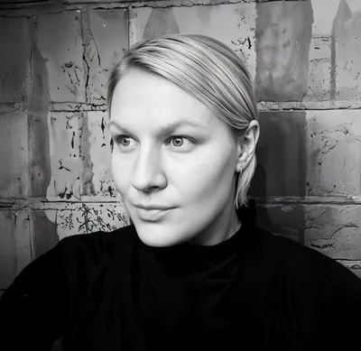 Black-and-white portrait of a blonde woman in a black turtleneck against a brick wall