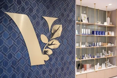 Gold letter V with floral detail on blue geometric tile wall beside shelved skincare products