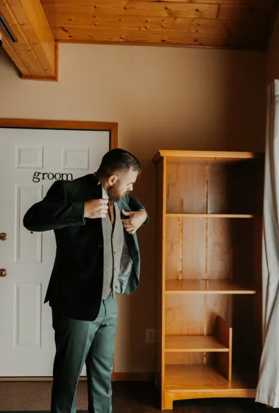 Groom adjusting his dark suit jacket in a wood-paneled getting-ready room